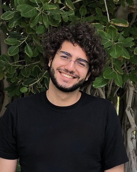 Mahan Fathi, smiling, in a black t-shirt in front of a leafy tree
